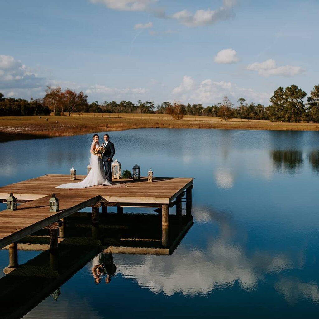 bride and groom standing on dock with lanterns next to large pond at legacy at oak meadows wedding venue